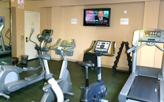 Una palestra con diverse macchine cardio, un televisore che mostra un telegiornale e un tapis roulant con schermo digitale.