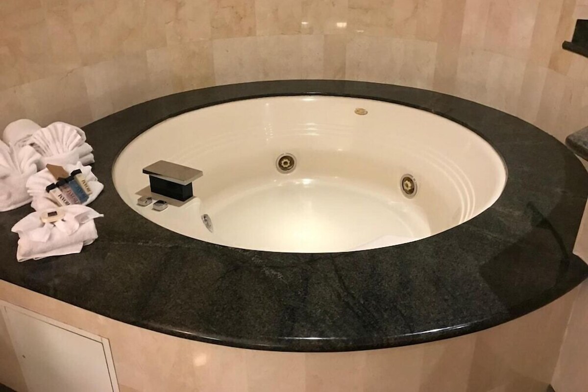 A round bathtub with a black marble surround, a small control panel, and a towel rack with towels.