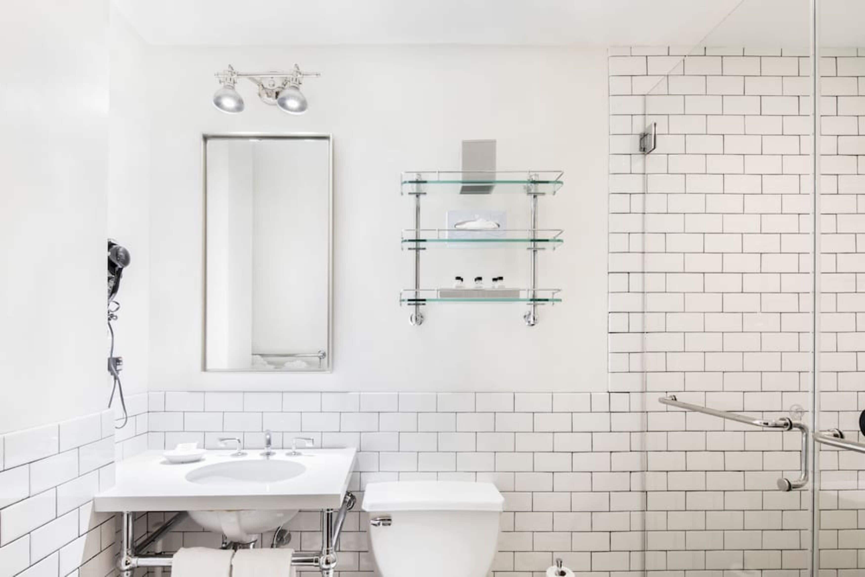Un baño moderno con un lavamanos blanco, espejo y repisas de vidrio.