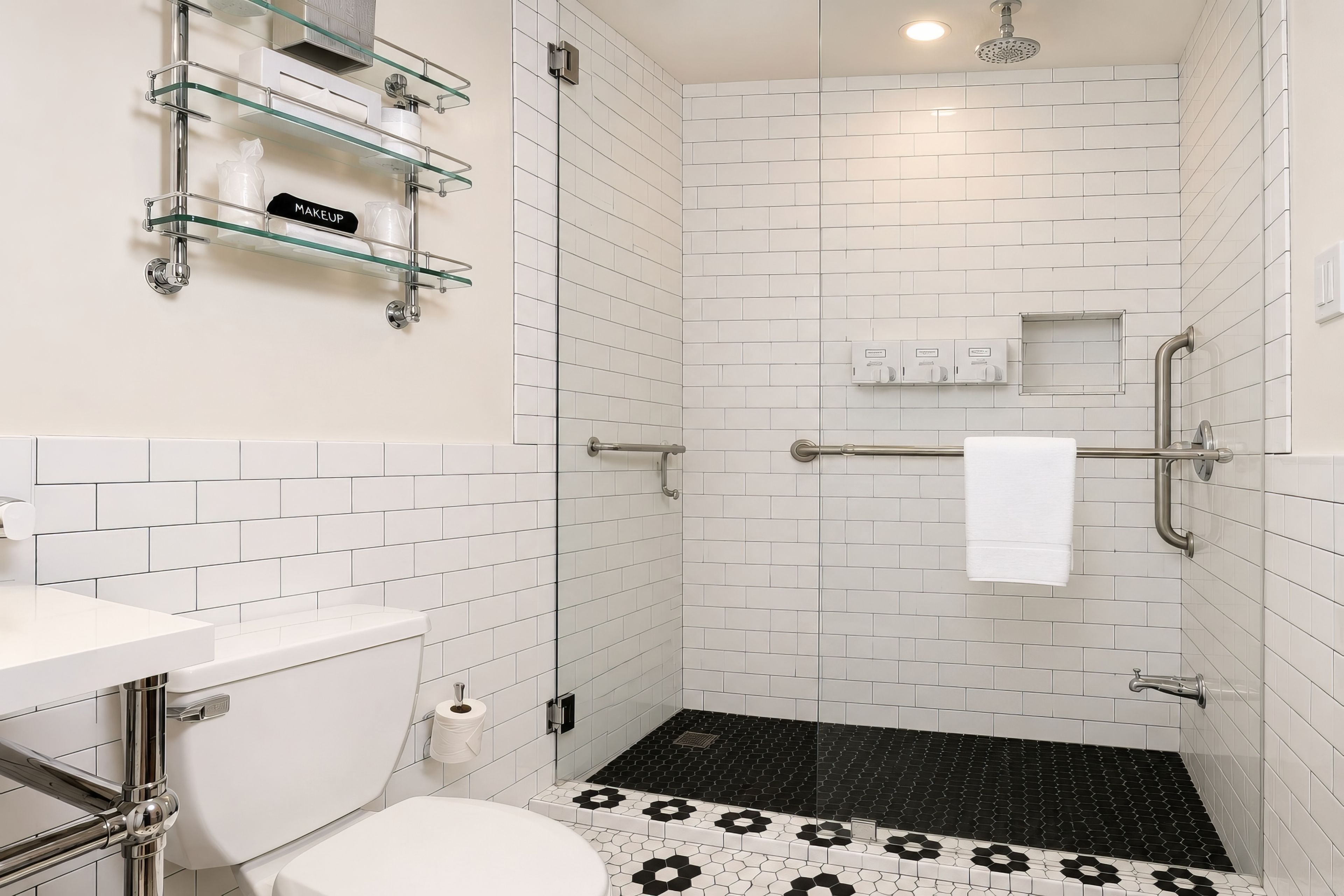 Un baño moderno con azulejos blancos tipo metro, cabina de ducha con mampara de vidrio, inodoro blanco y alfombrilla de ducha con estampado blanco y negro.