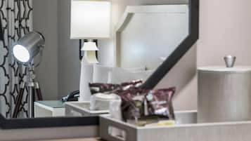 A hotel room with a large mirror, a desk with a lamp, a framed picture on the wall, and a tray with snacks.