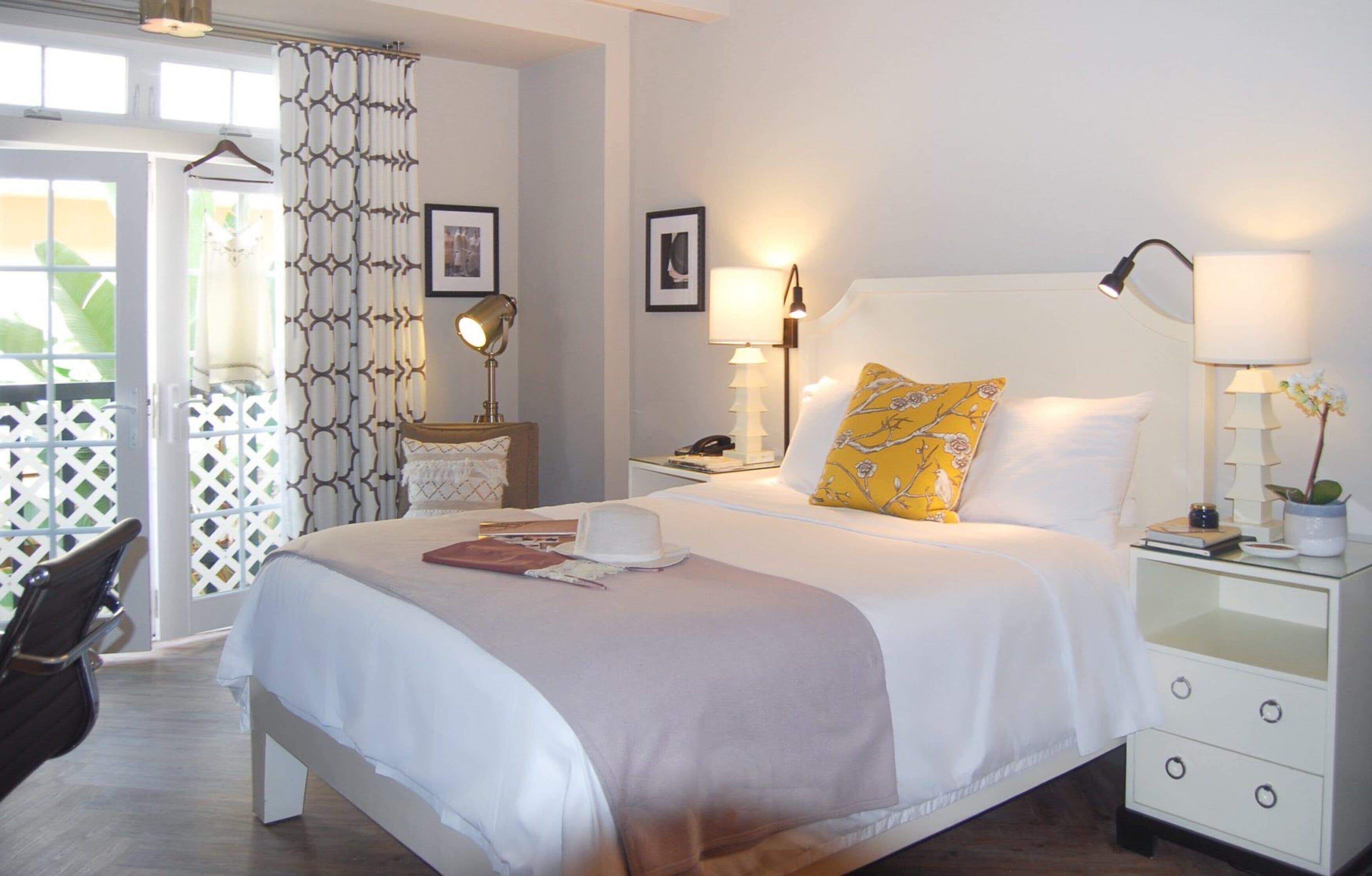 Habitación de hotel ordenada con cama, mesitas de noche, lámparas y vistas a través de una ventana.