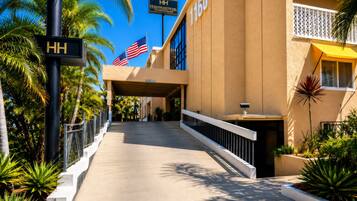 A hotel entrance with a palm tree-lined pathway, an American flag, and a sign for the Hollywood Hotel.