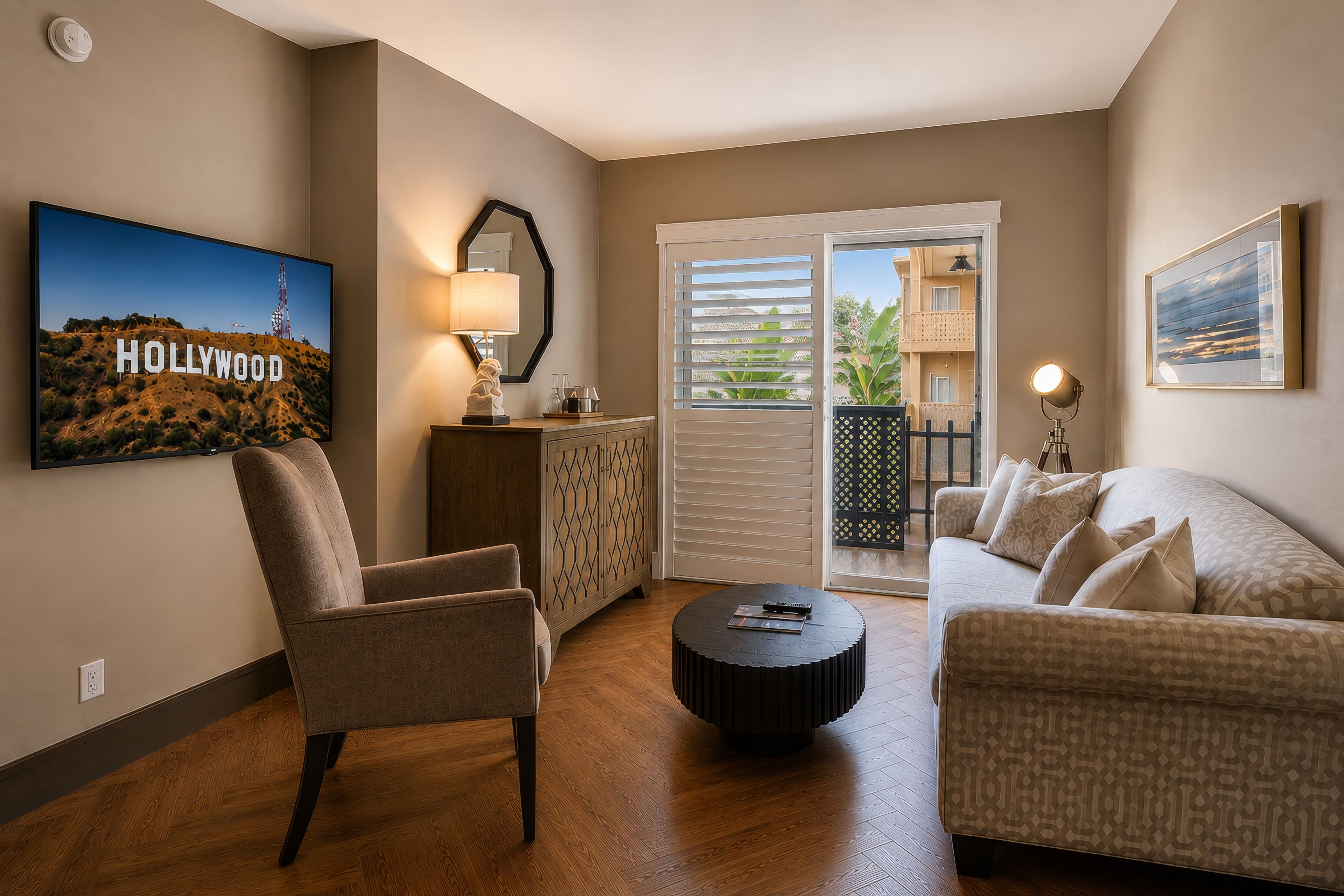 Ein Wohnzimmer mit Sofa, Sessel und Couchtisch. Man sieht ein Bild der Hollywood-Schrift, eine Lampe und eine Aussicht durch eine Schiebetür.