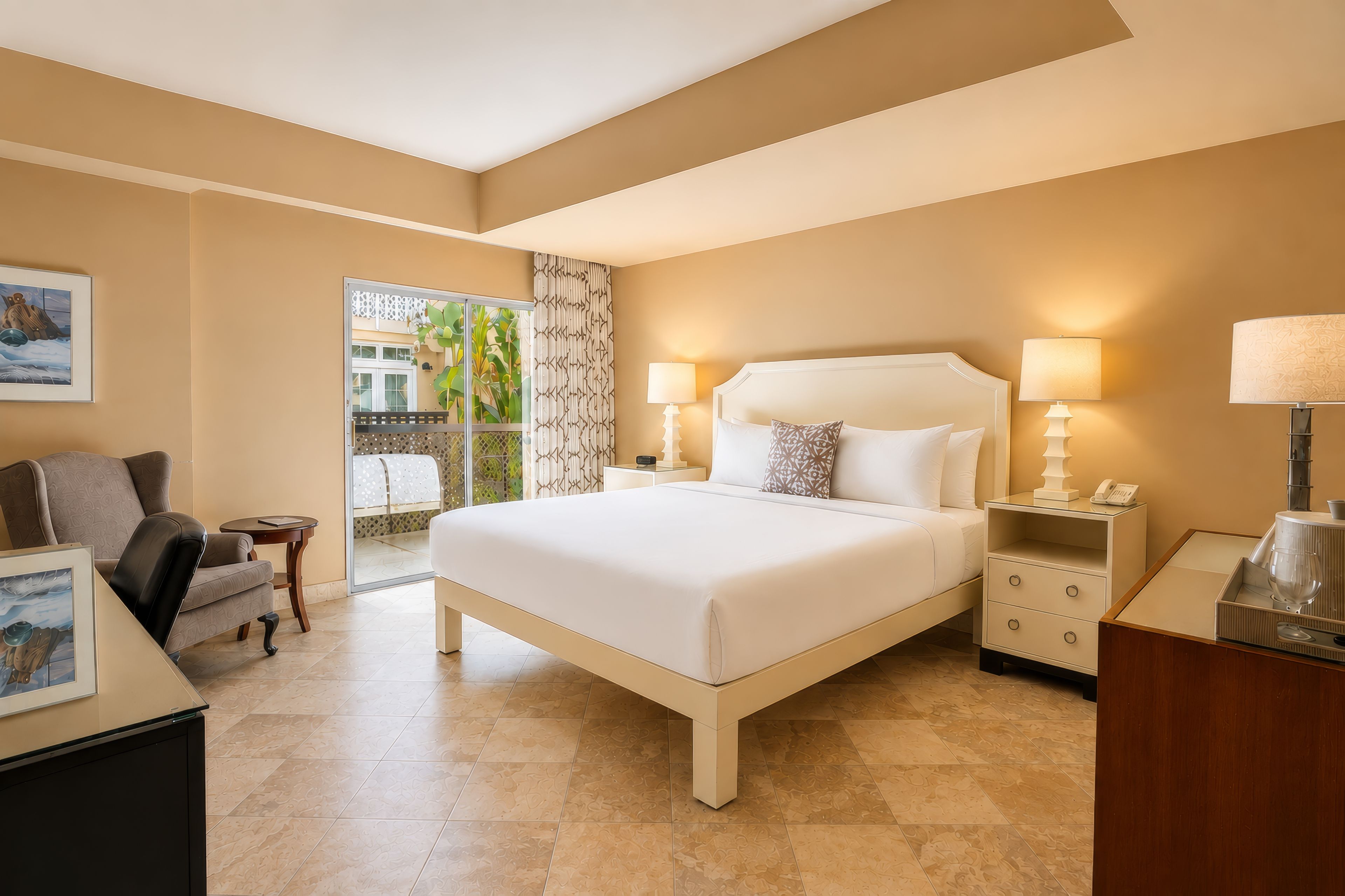 A hotel room with a large bed, two bedside tables with lamps, a small desk, and a chair.