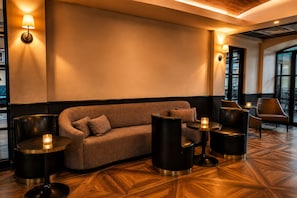 A modern lounge area with a sofa, round tables, and chairs, featuring a geometric patterned floor and warm ambient lighting. - Hollywood Hotel (Los Angeles)