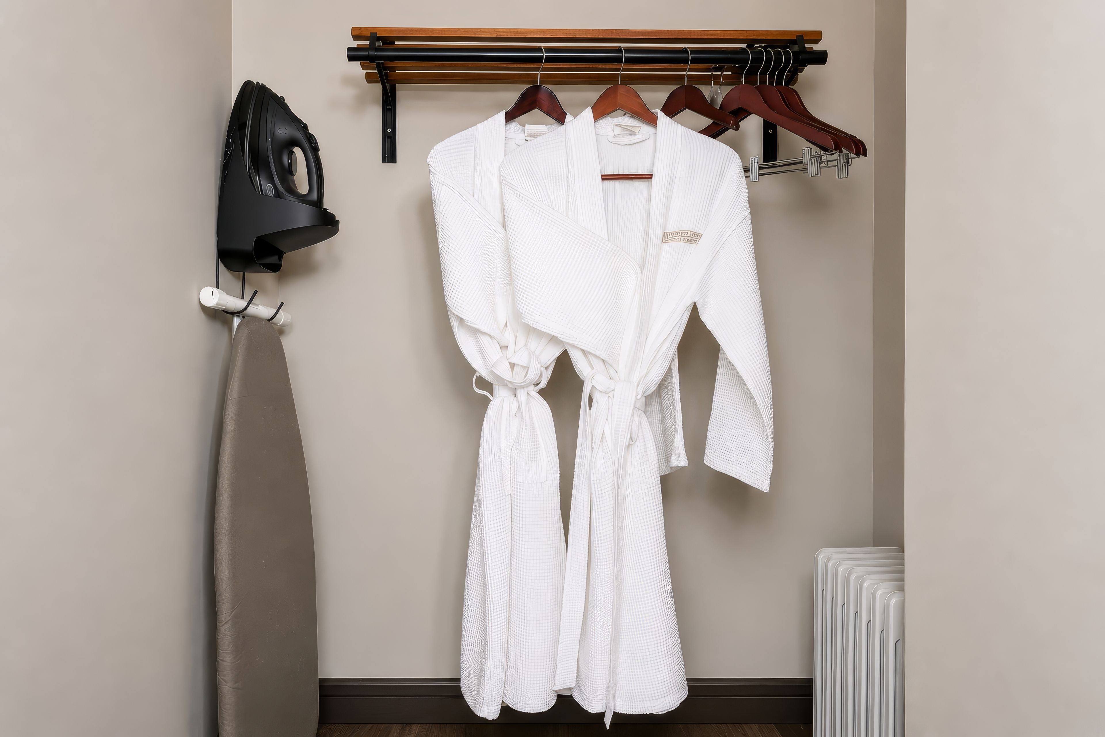 Habitación de hotel con una bata colgada en un perchero de madera, un secador de pelo en un soporte de pared y un radiador.