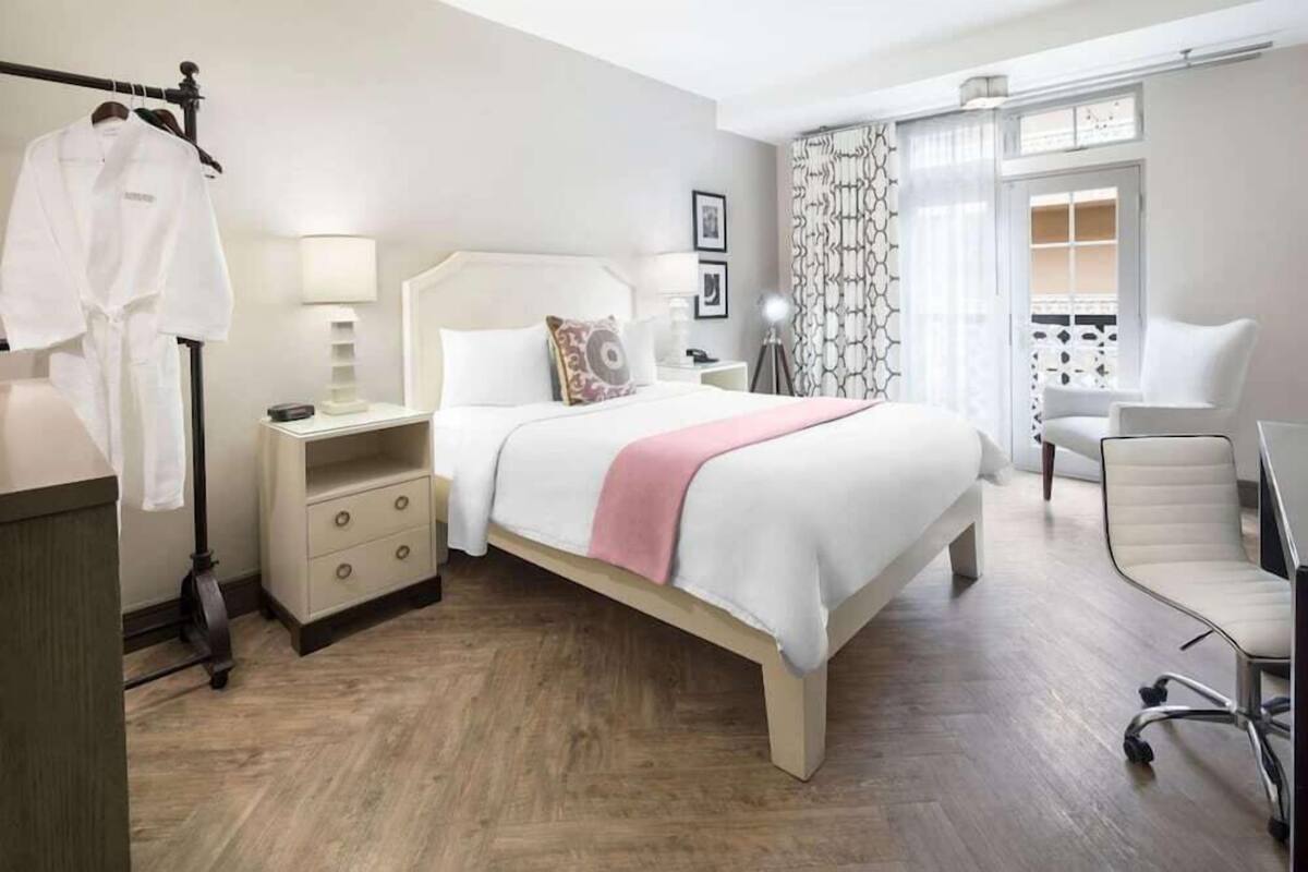 A hotel room with a bed, bedside table, lamp, chair, and a view of the balcony.