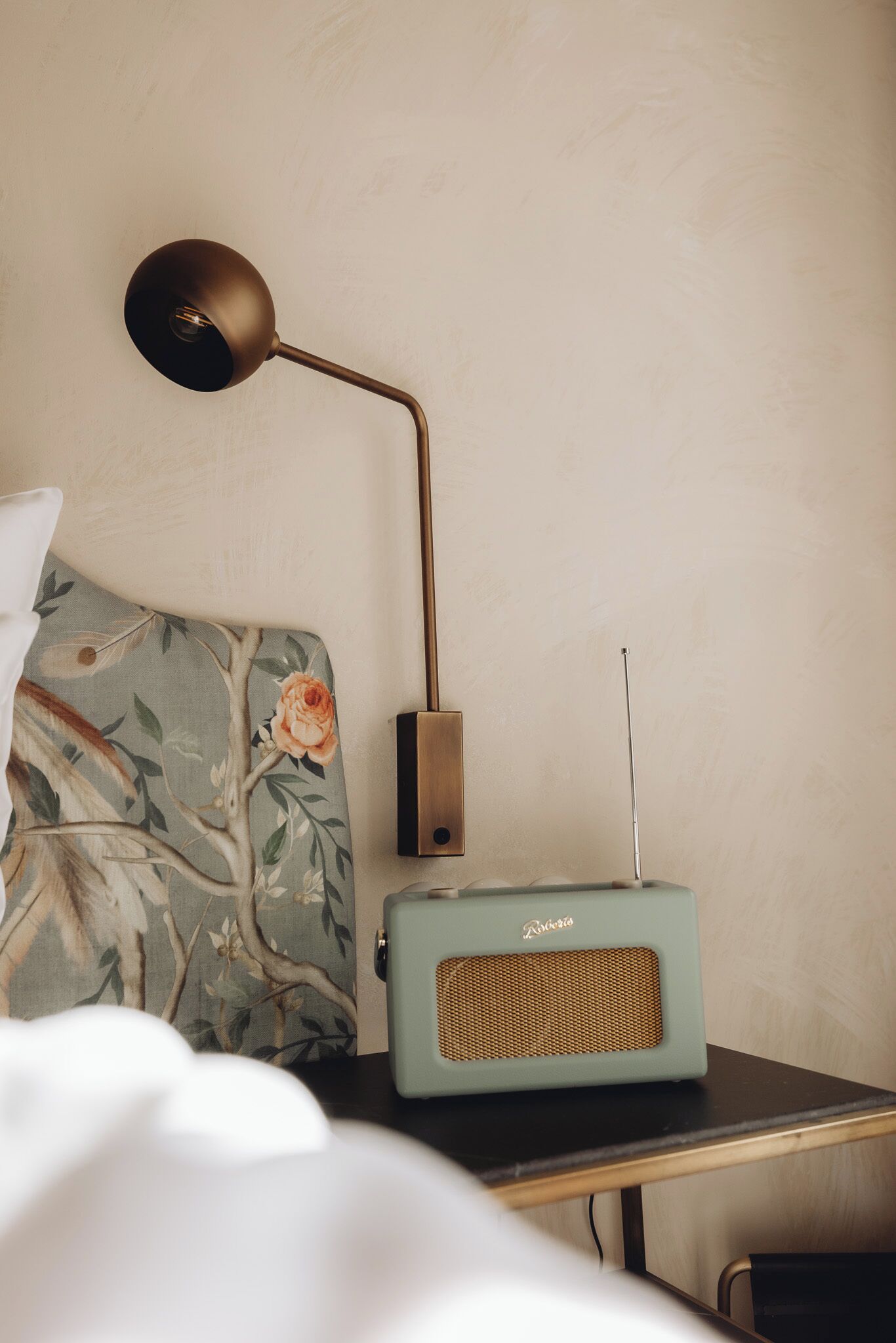 A bed with a floral-patterned headboard, a vintage-style radio, and a modern desk lamp.