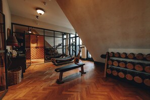 A gym with wooden flooring, exercise equipment, and a wall-mounted dumbbell rack.