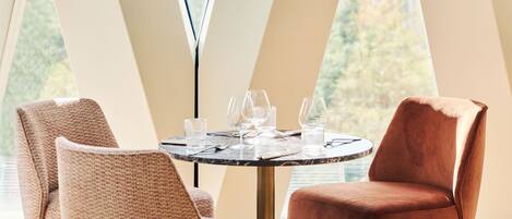 A dining area with a round table, two chairs, and a view of a cityscape through large windows.