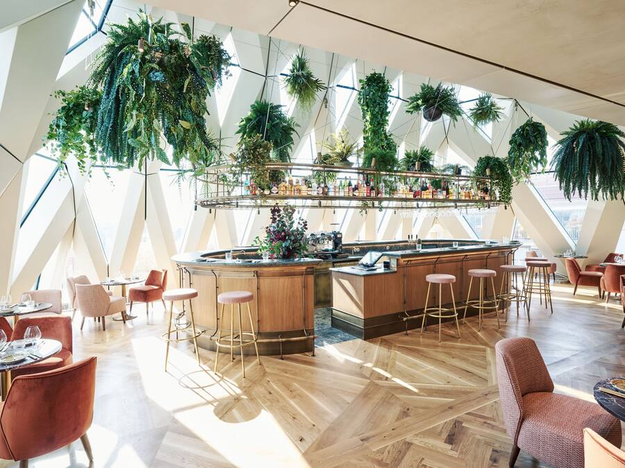 A modern restaurant with a central bar, high ceilings, and hanging plants.