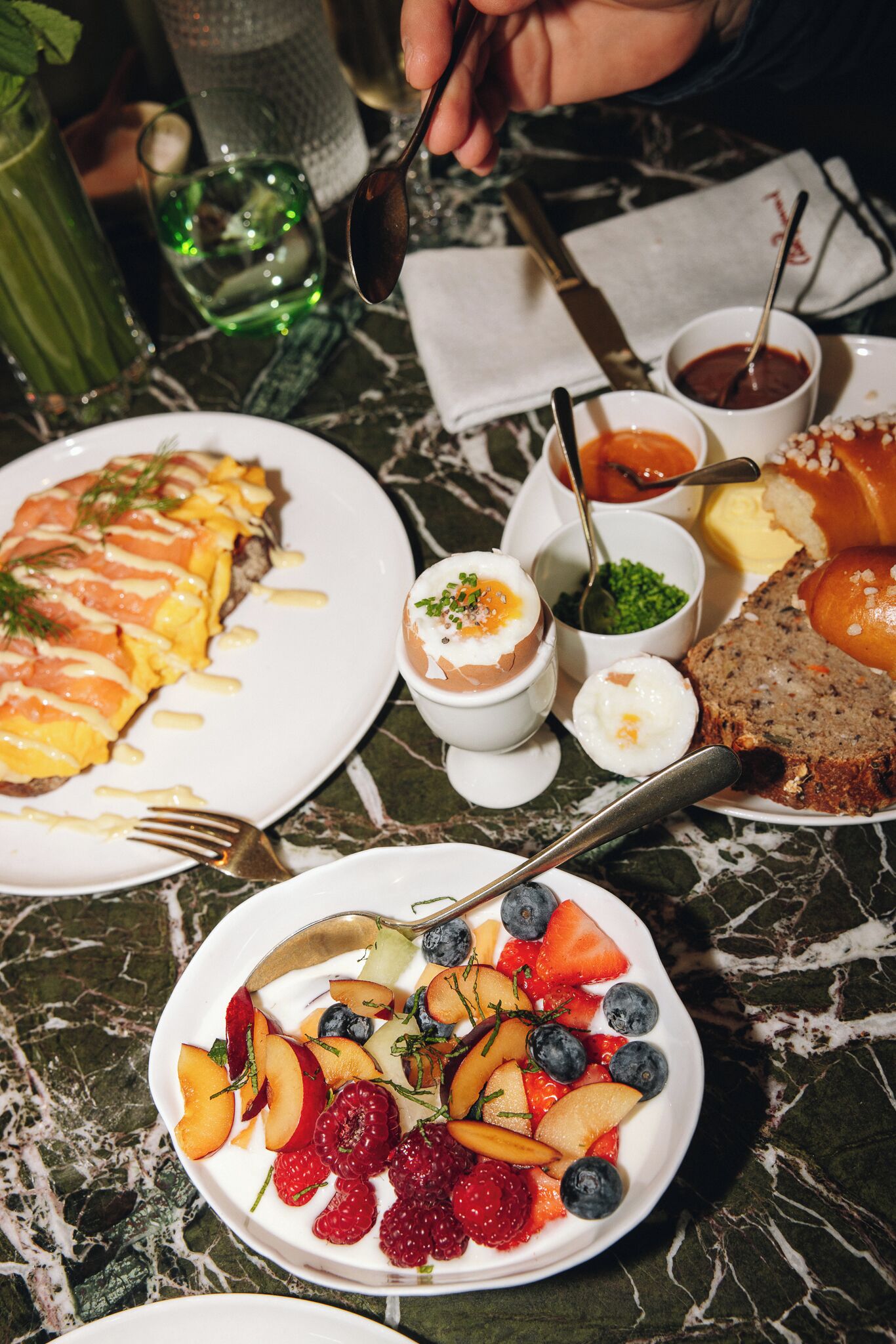 A dining table with various dishes, including a plate of salmon, a bowl of fruit, and a slice of bread.