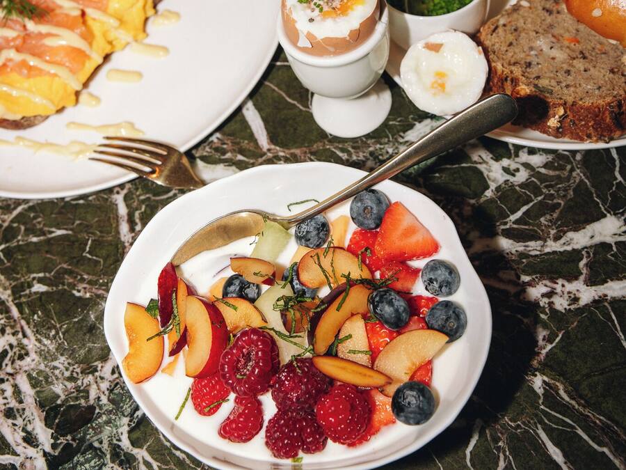 A dining table with various dishes, including a plate of salmon, a bowl of fruit, and a slice of bread.