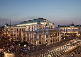 A large, historic building with a prominent dome and classical architecture, situated at a city intersection with visible traffic.
