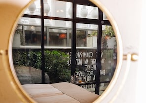A circular window with a view of a room featuring a bed, a table with a glass, and a potted plant.