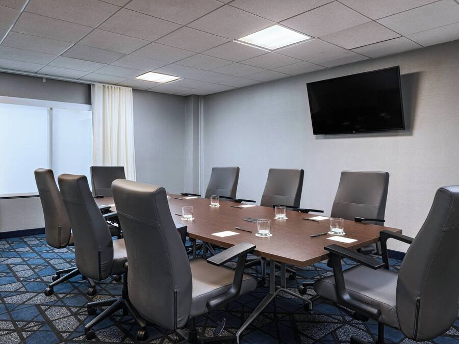 Un salón de conferencias con una larga mesa, ocho sillas y un televisor de pantalla plana en la pared.