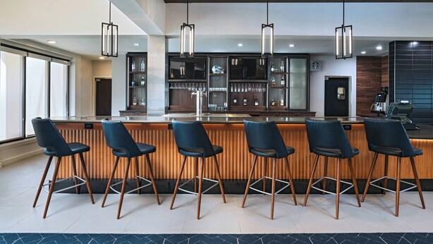 A modern bar area with wooden bar counters, black bar stools, and pendant lighting.