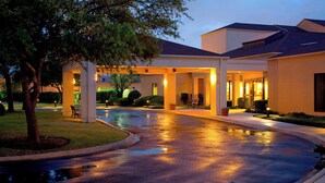 A hotel entrance with a covered walkway, a wet driveway, and a tree in the foreground.