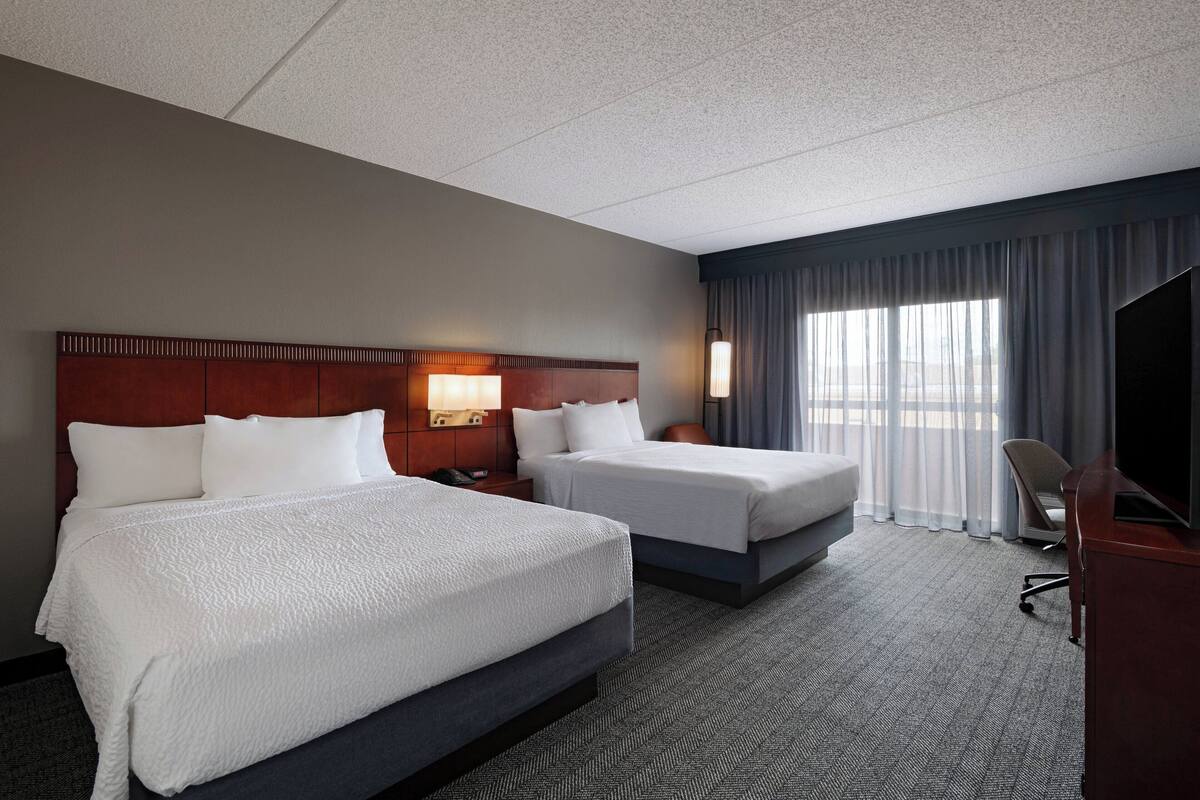A hotel room with two beds, a desk, a chair, and a TV.