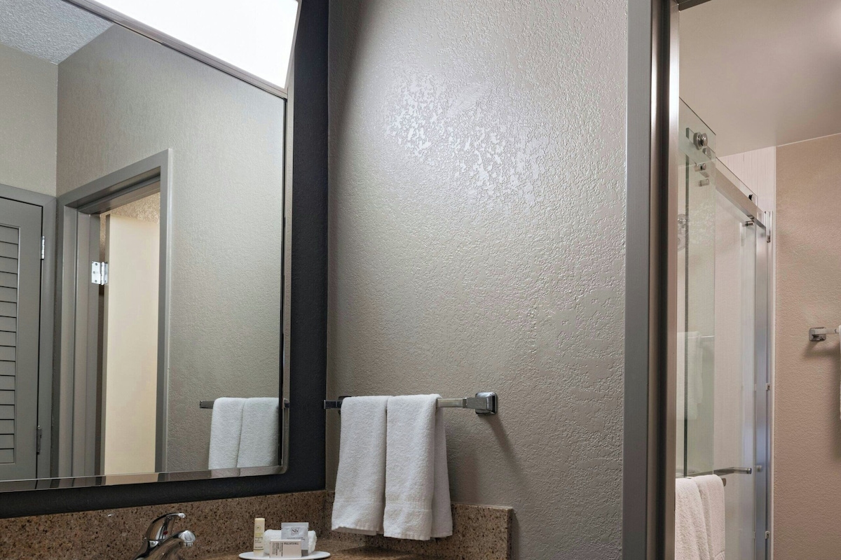A modern bathroom with a granite countertop, a large mirror, a glass shower enclosure, and a towel rack.