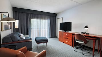 A hotel room with a sofa, a desk, a television, and a lamp.