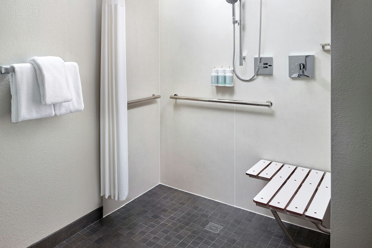 A modern bathroom with a shower, a towel rack, a handrail, and a small table.