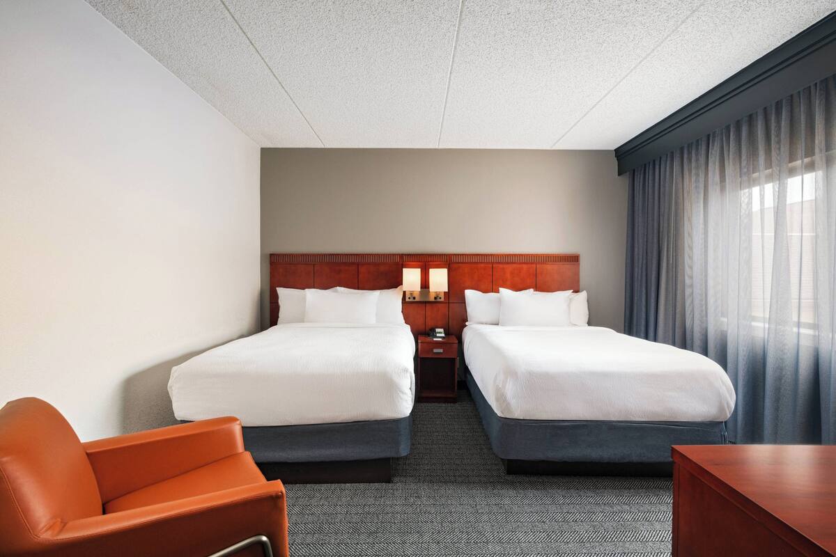 A hotel room with two beds, a wooden headboard, a nightstand, a desk, and a chair.