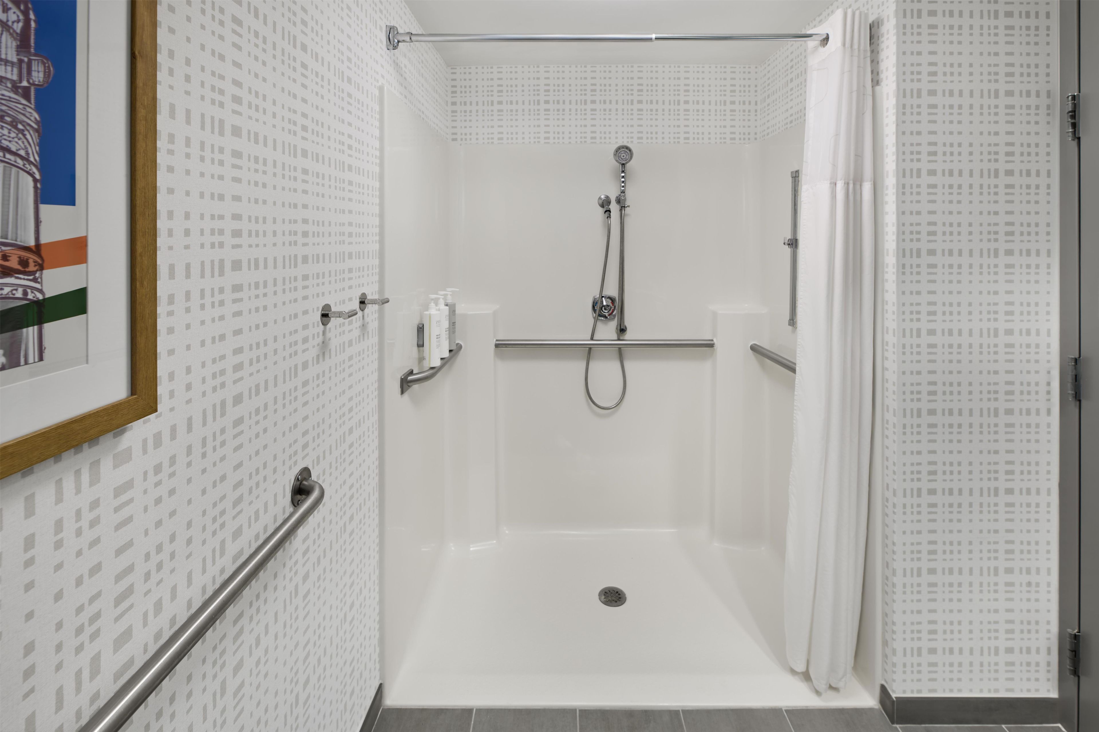 A walk-in shower with a handrail, a showerhead, and a tiled floor.