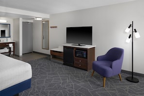 A hotel room with a bed, a desk with a flat-screen TV, a microwave, a chair, and a floor lamp. - Hampton Inn Janesville (Janesville)