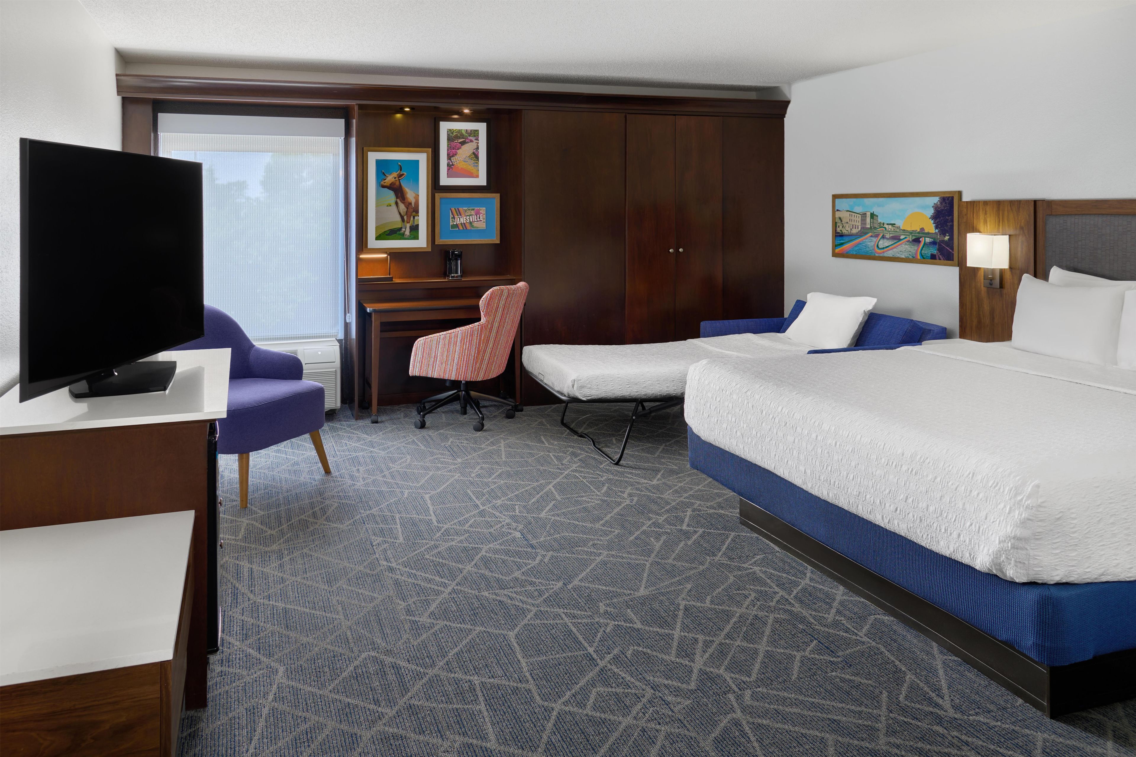 Habitación de hotel con una cama grande, un escritorio con silla, televisión y obras de arte en las paredes.