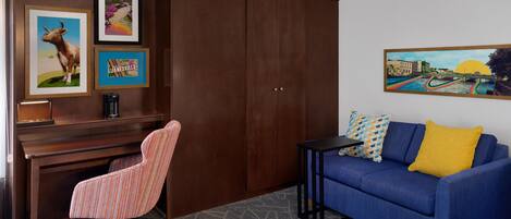 A room with a desk, a chair, a sofa, and a bed. There are framed pictures on the wall.