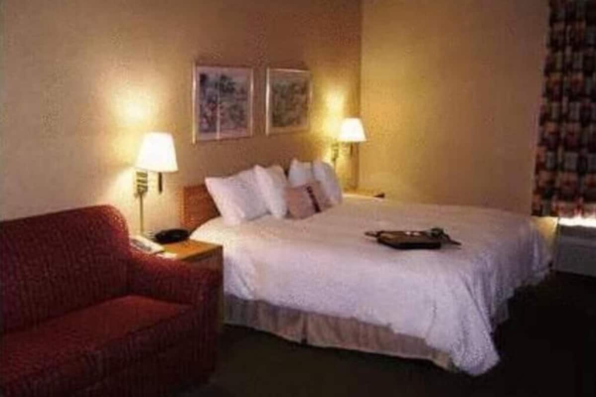 A hotel room with a bed, two bedside lamps, a red chair, and two framed pictures on the wall.