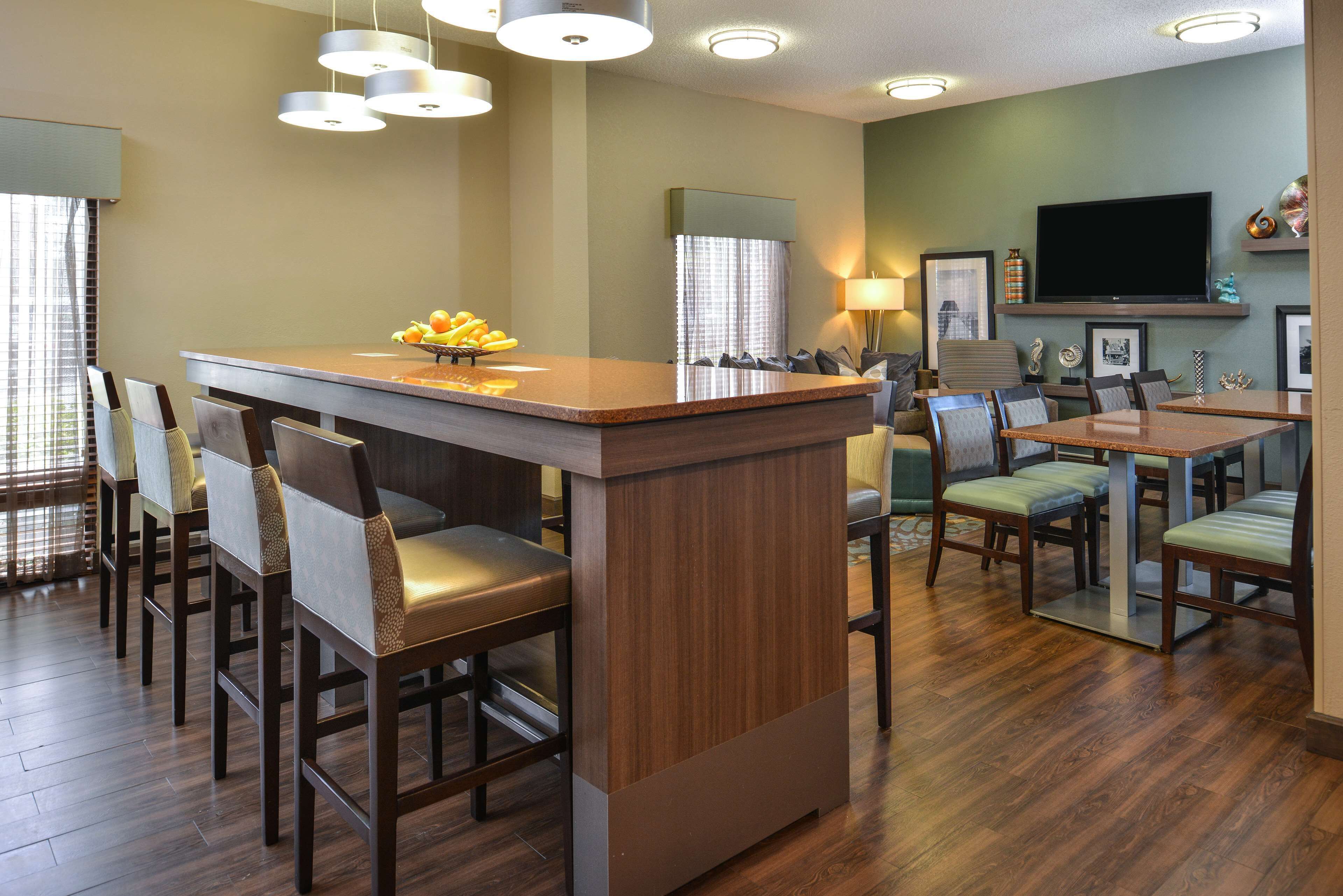 A modern kitchen with a central island, dining area with chairs, and a flat-screen TV mounted on the wall.