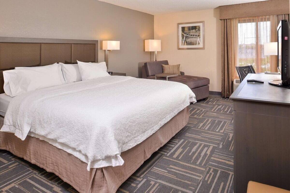 A hotel room with a large bed, a desk with a computer, and a chair.