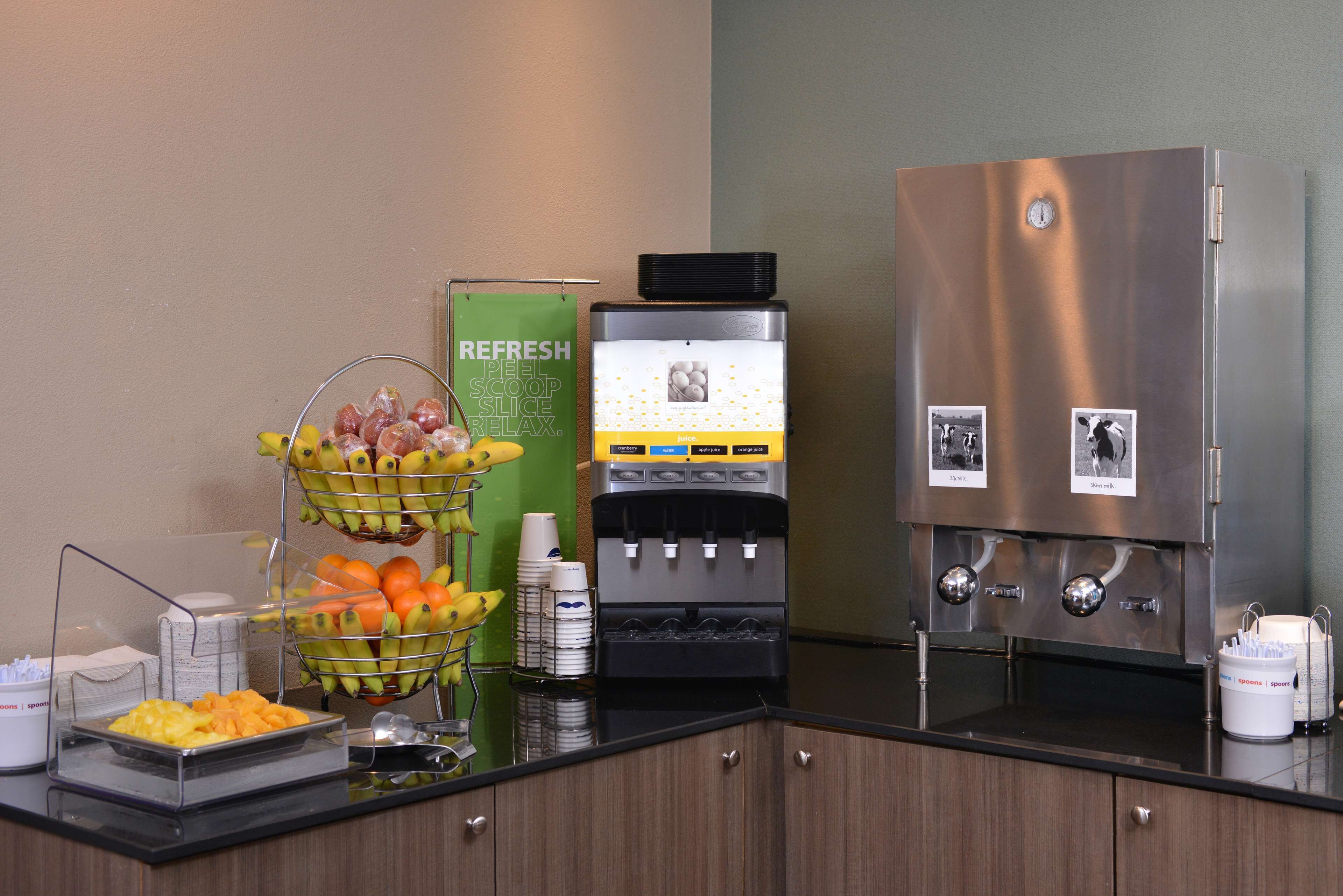 A buffet setup with a fruit and juice station, a refrigerator, and a coffee maker.
