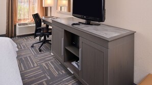 Ein Hotelzimmer mit einem Bett, einem Schreibtisch mit Flachbildfernseher, einem Sessel, einer Lampe und einem Vorhangfenster.