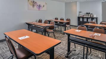A conference room with multiple tables and chairs, a coffee station, and a decorative wall piece.