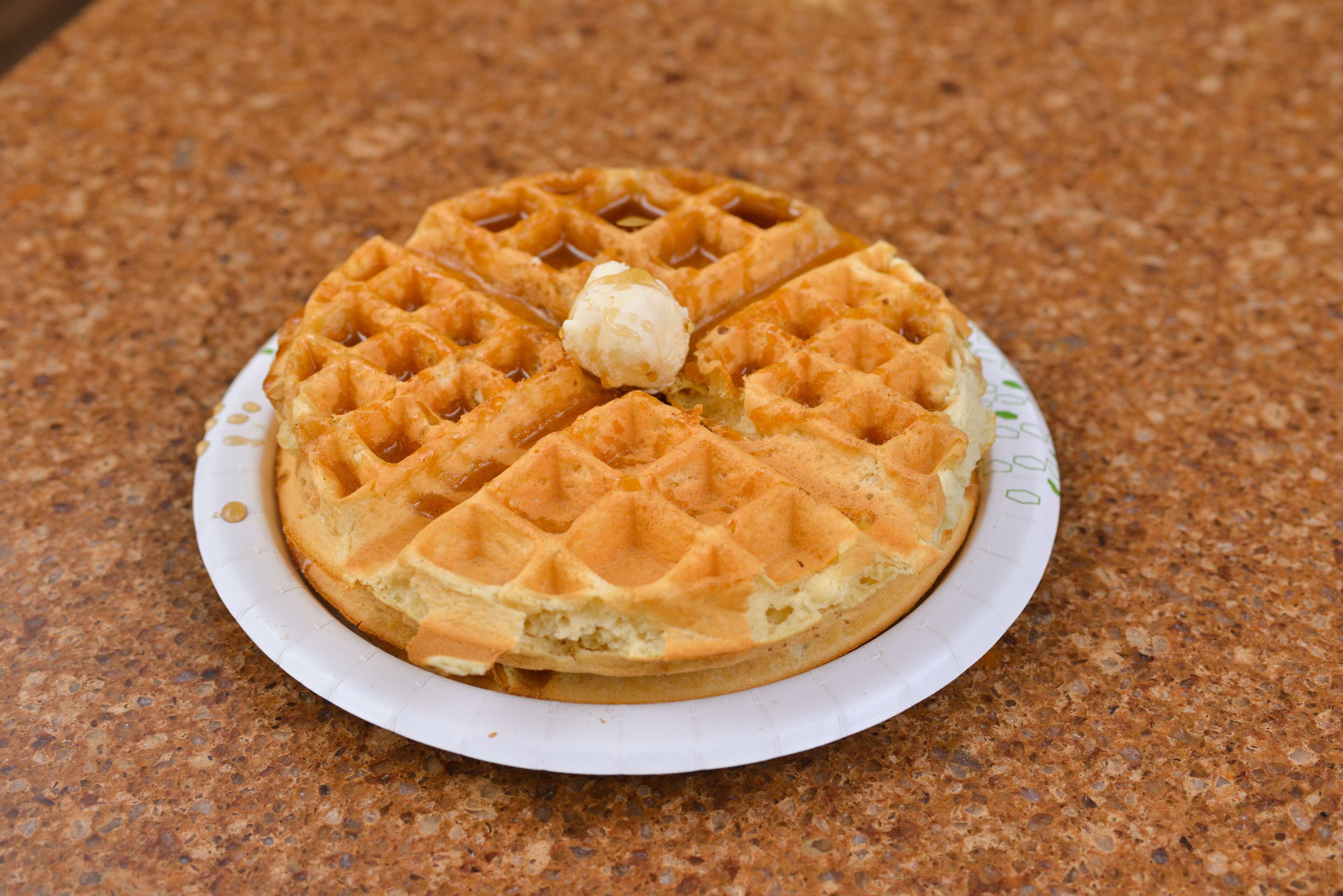 A waffle with a dollop of cream on a paper plate.