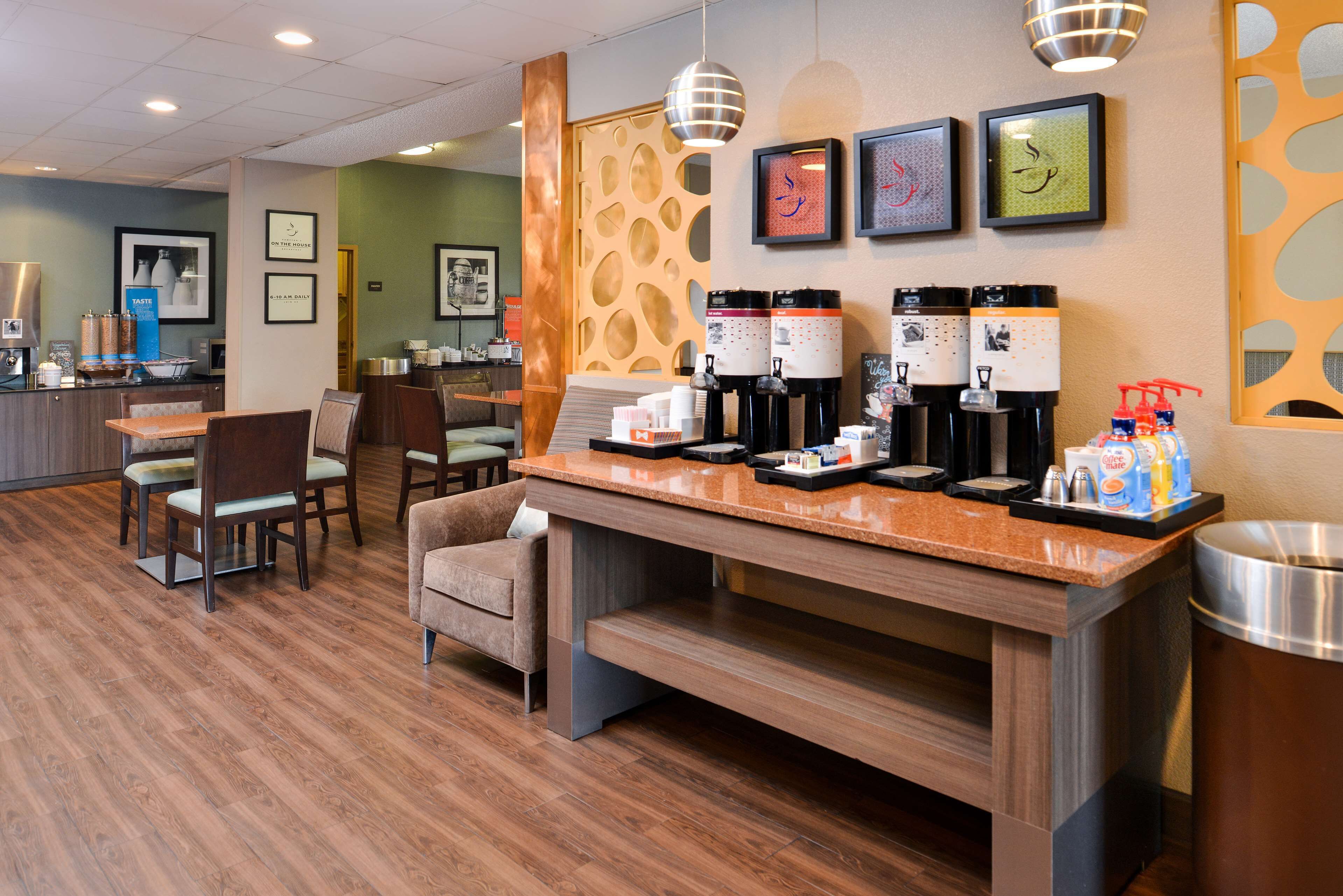 Un vestíbulo de hotel con una estación de café, zona de estar y un mostrador de recepción.