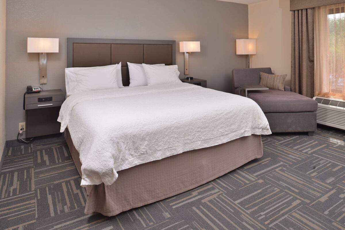 A hotel room with a large bed, two bedside tables with lamps, a chair, and a window with curtains.