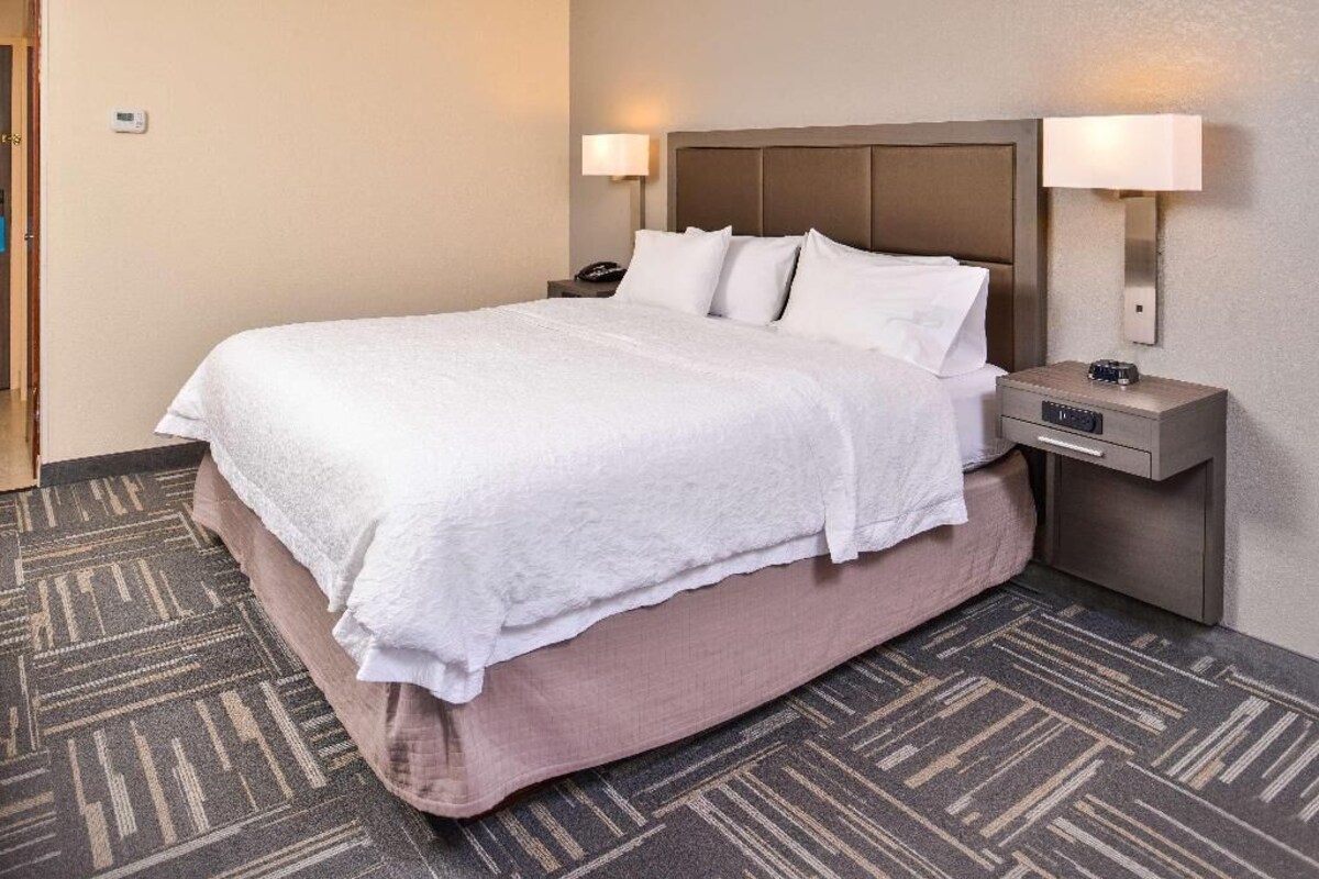 A hotel room with a large bed, two bedside tables, and a wall-mounted lamp.