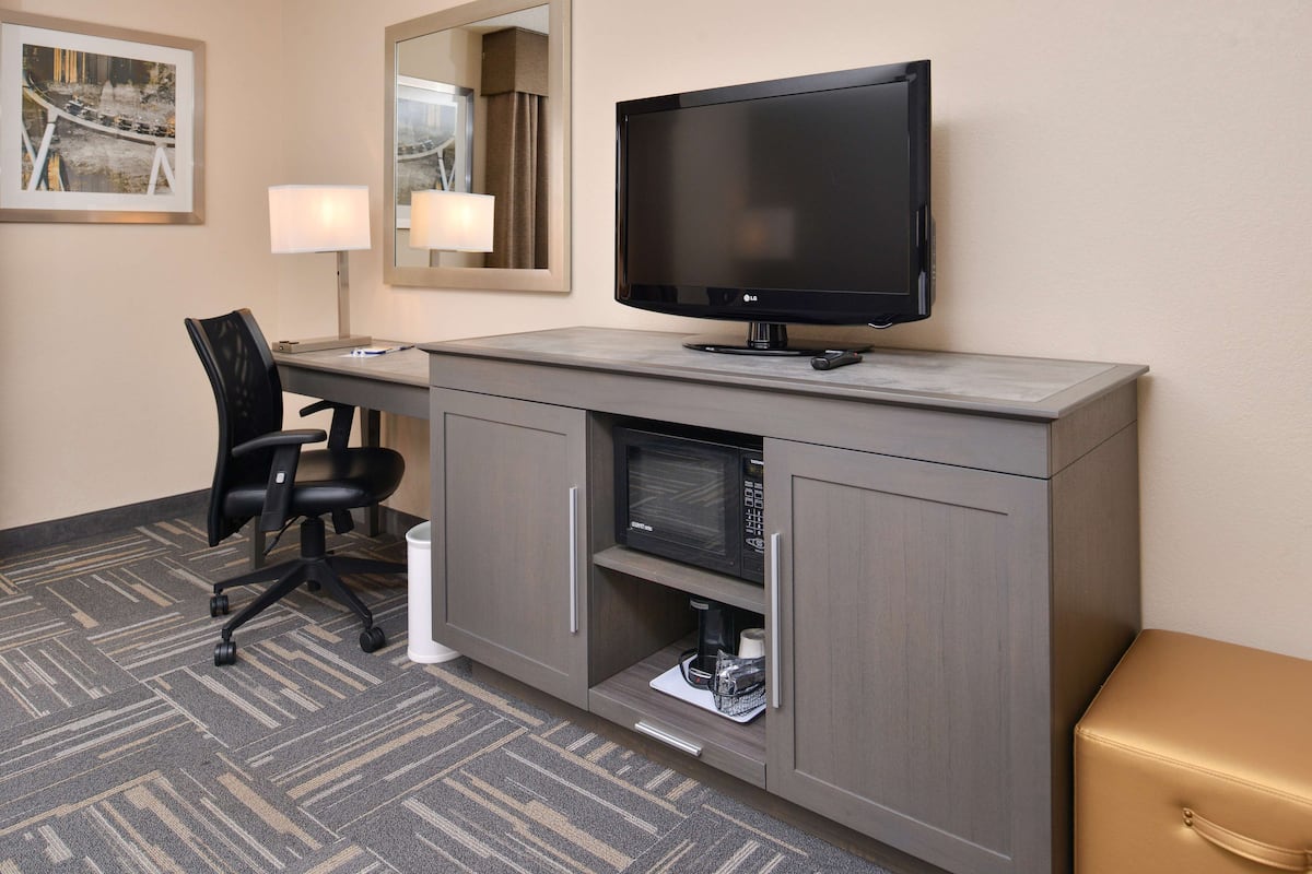 A hotel room with a desk, chair, television, microwave, and a small cabinet.