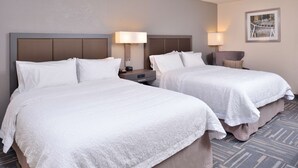 Ein Hotelzimmer mit zwei Betten, jeweils mit weißer Bettwäsche, Kopfteilen, Nachttischen mit Lampen und einem Teppichboden.