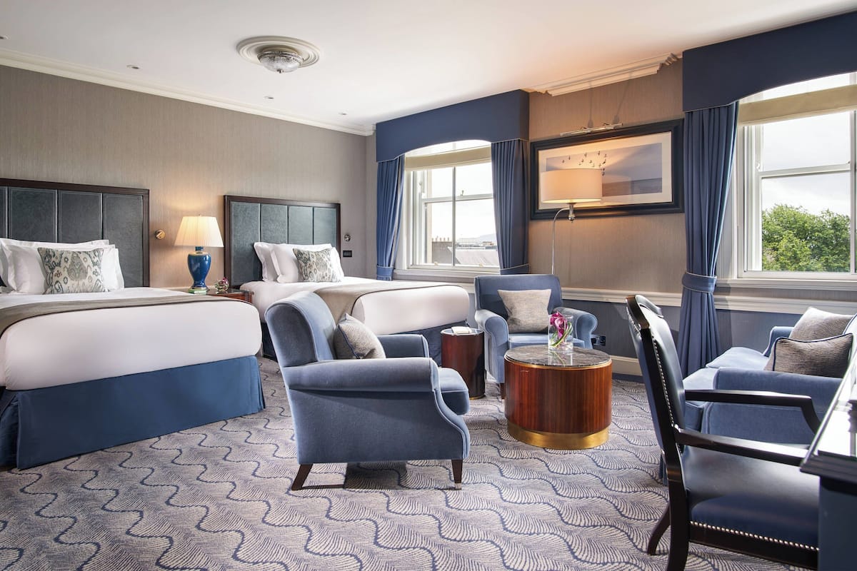 Habitación de hotel con una cama grande, dos sillones, un sofá, una mesita redonda y un televisor.