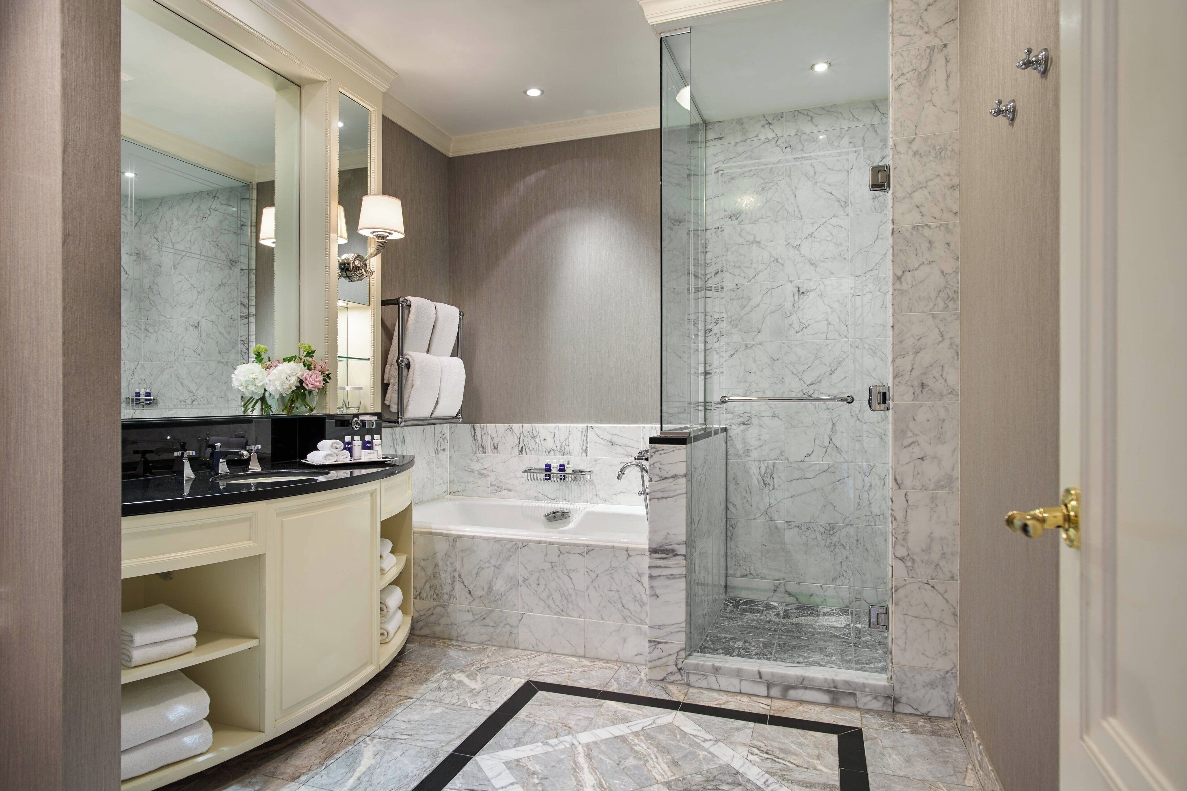 A modern bathroom with a marble sink, a bathtub, and a glass-enclosed shower.