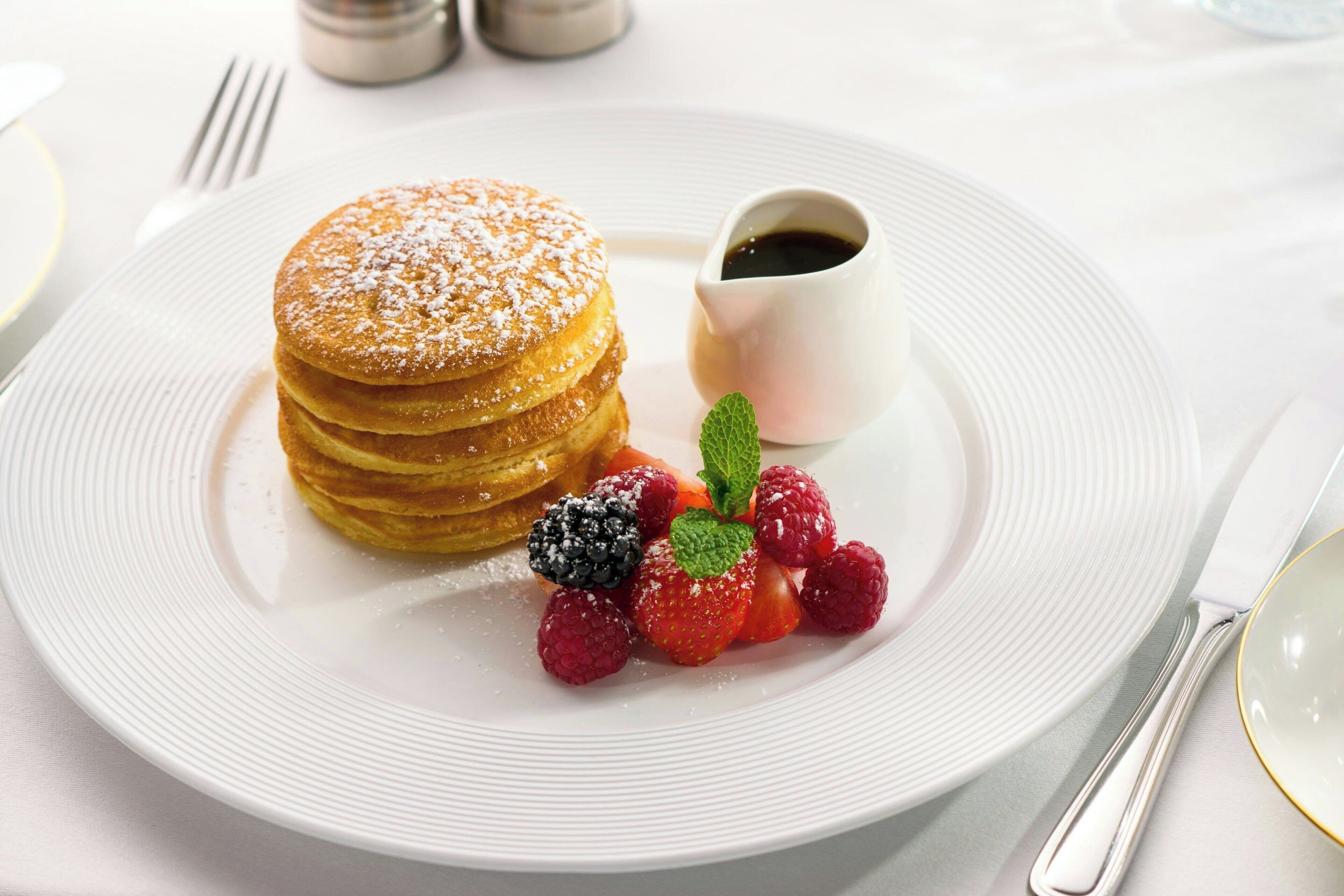 Ein Teller mit Pfannkuchen, eine kleine Tasse Ahornsirup und frischen Beeren.