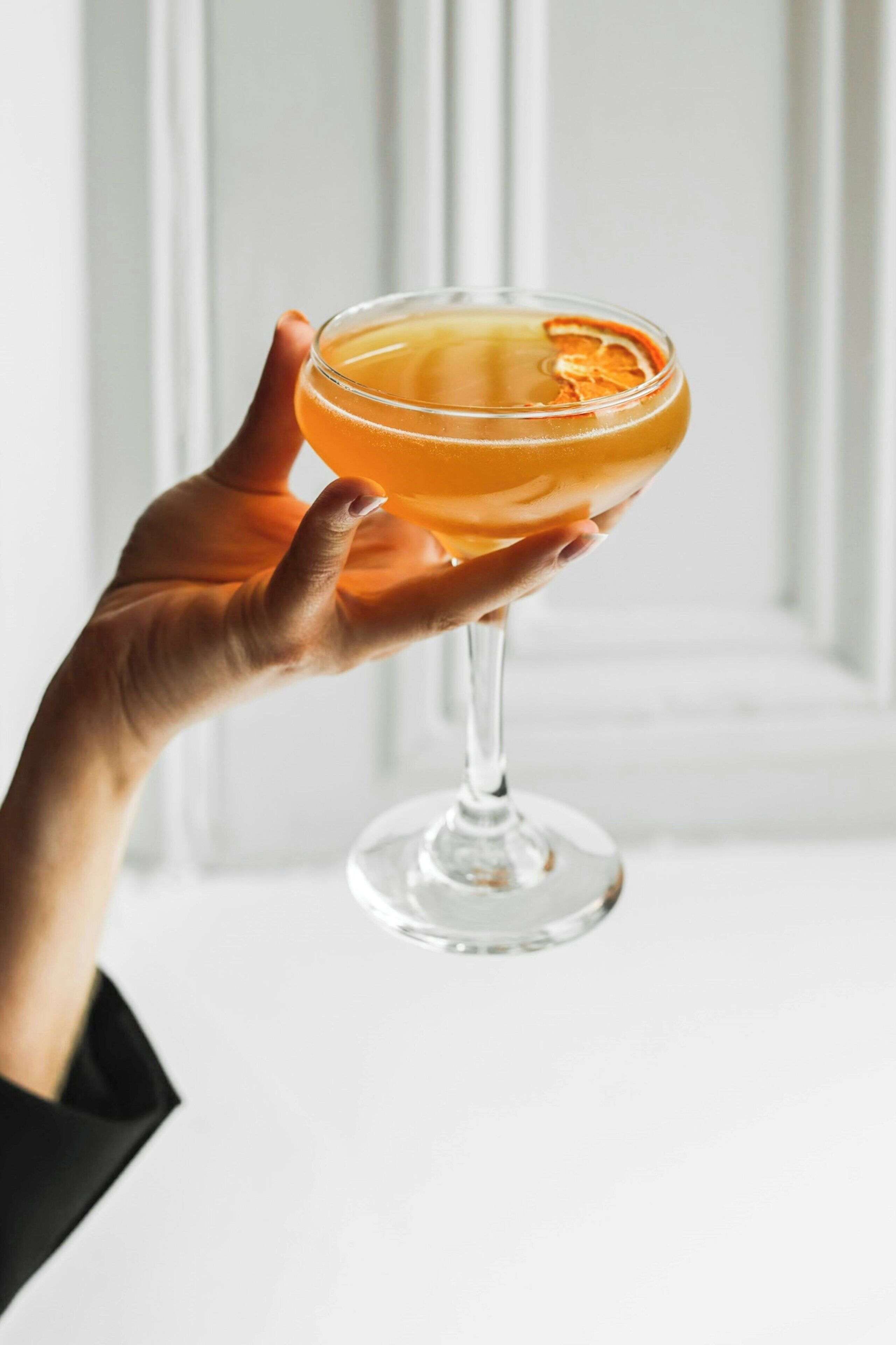 Een hand die een cocktailglas vasthoudt, versierd met citrus.