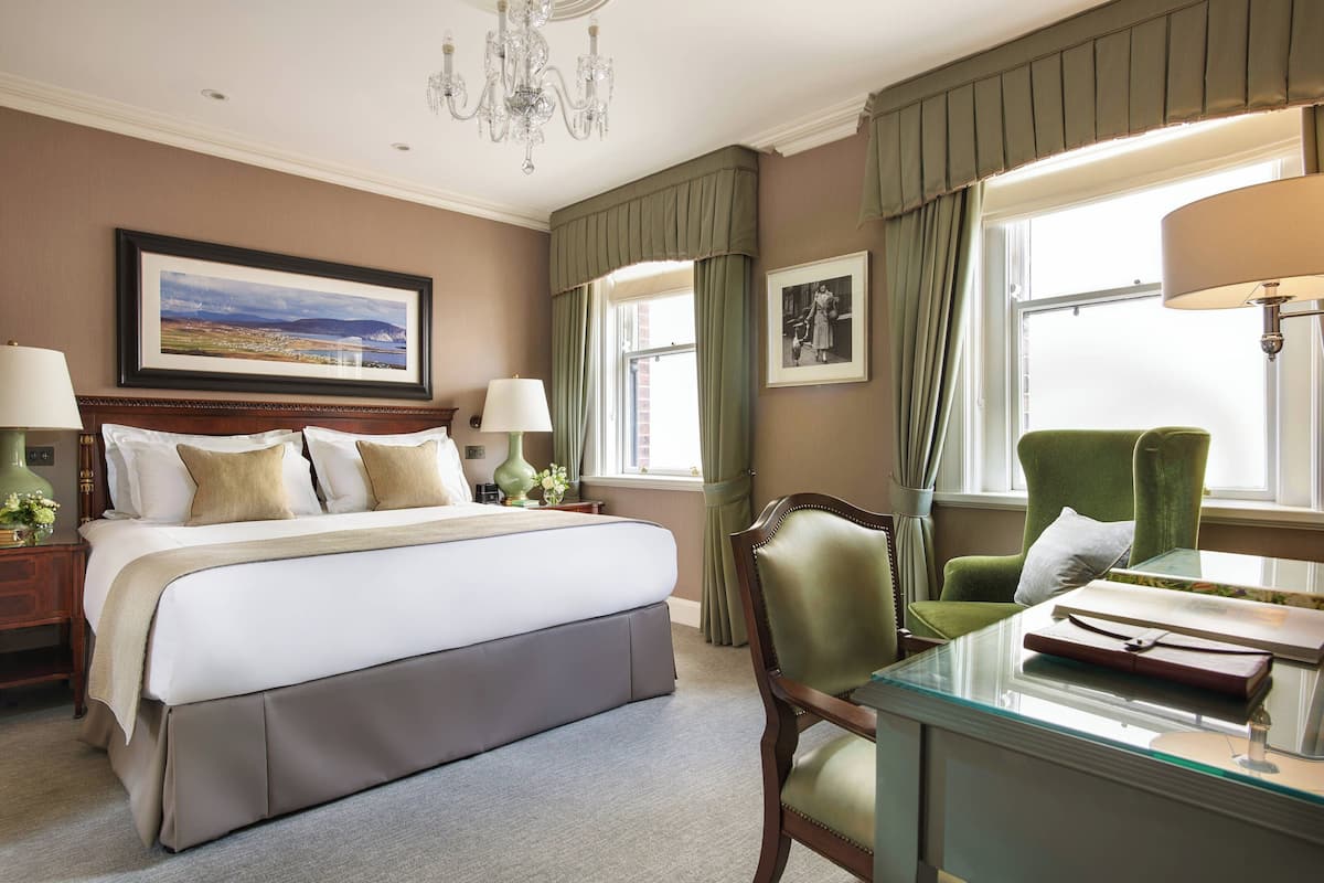 Una habitación de hotel con una cama grande, un escritorio con lámpara, una silla y una ventana con cortinas.