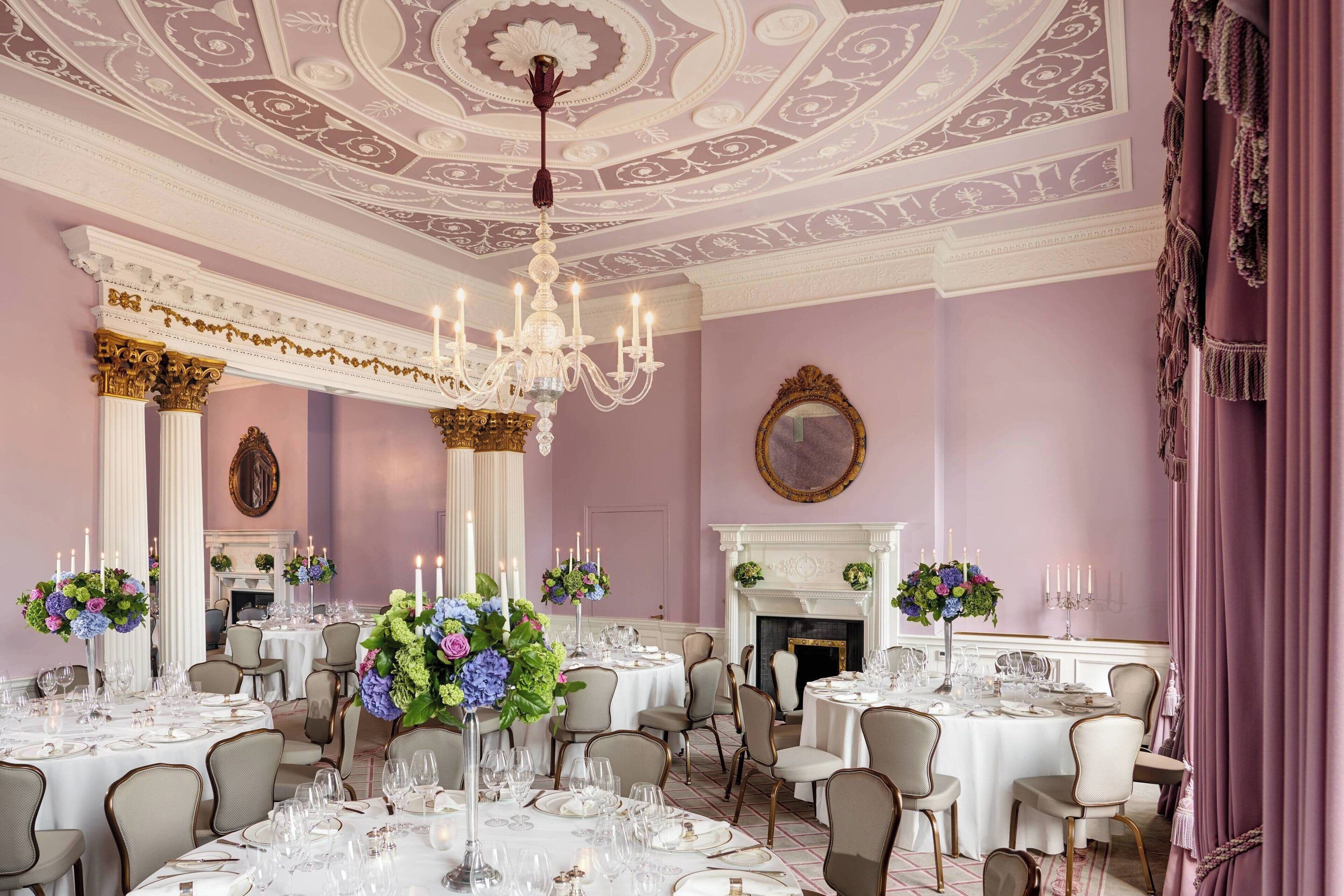 A formal dining room with multiple round tables set for a meal, elegant chandeliers, and classic architectural details.